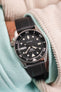 Hand in a hoodie pocket wearing a cream cord shirt with a black dial seiko 5 sports dive watch on a black rubber fkm dive strap