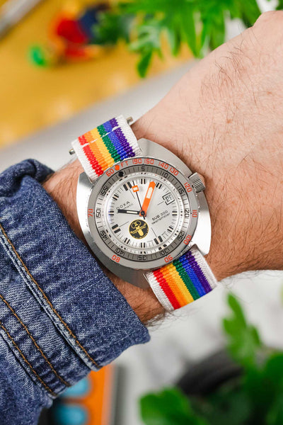 Close up wrist shot of a Doxa Sub 300 Dive watch fitted to a colourful rainbow striped elastic watch strap